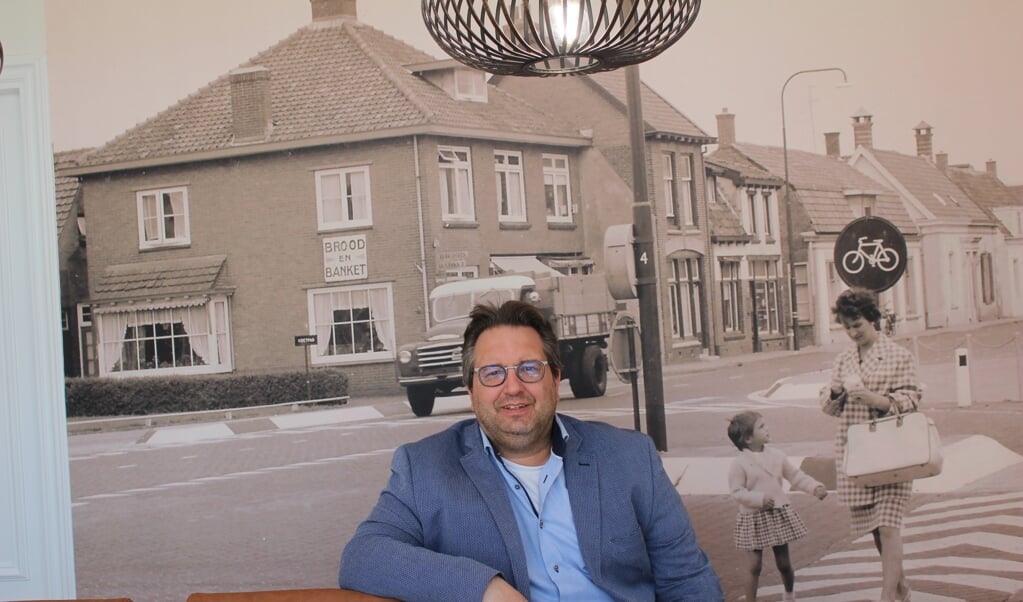 Makelaar Erwin Geijtenbeek in zijn spreekkamer met op de achtergrond historische foto van Dorpsstraat 3