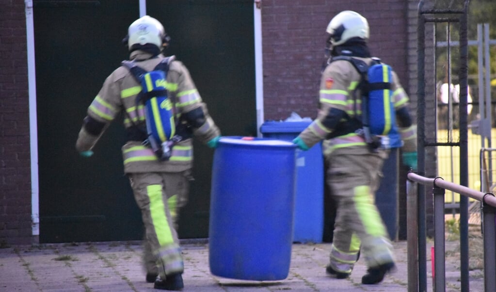 Brandweerlieden zetten de ton met vloeistof op een plek waar niemand er bij kan.