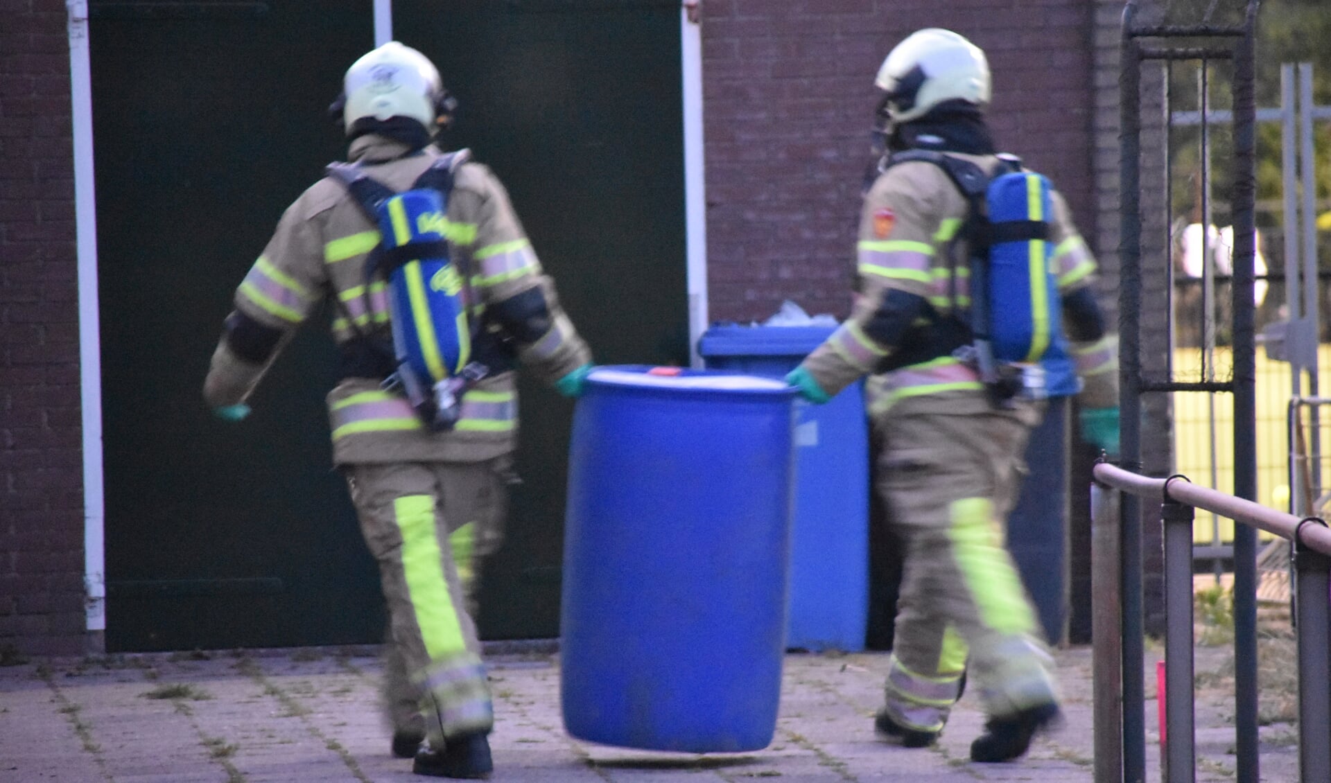 Brandweerlieden zetten de ton met vloeistof op een plek waar niemand er bij kan.