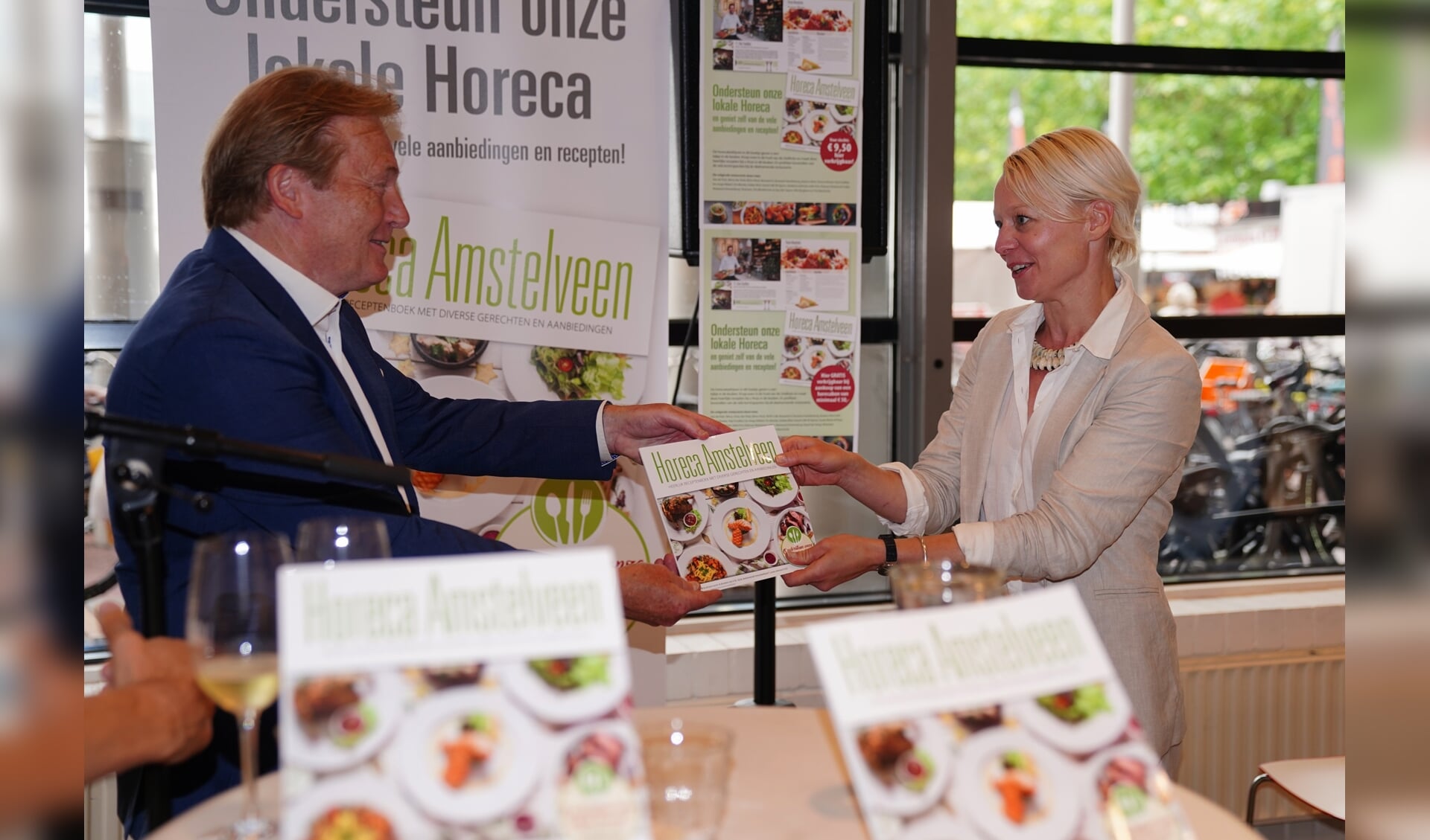 Michel Becker overhandigt het eerste exemplaar van Horeca Amstelveen aan wethouder Floor Gordon. 