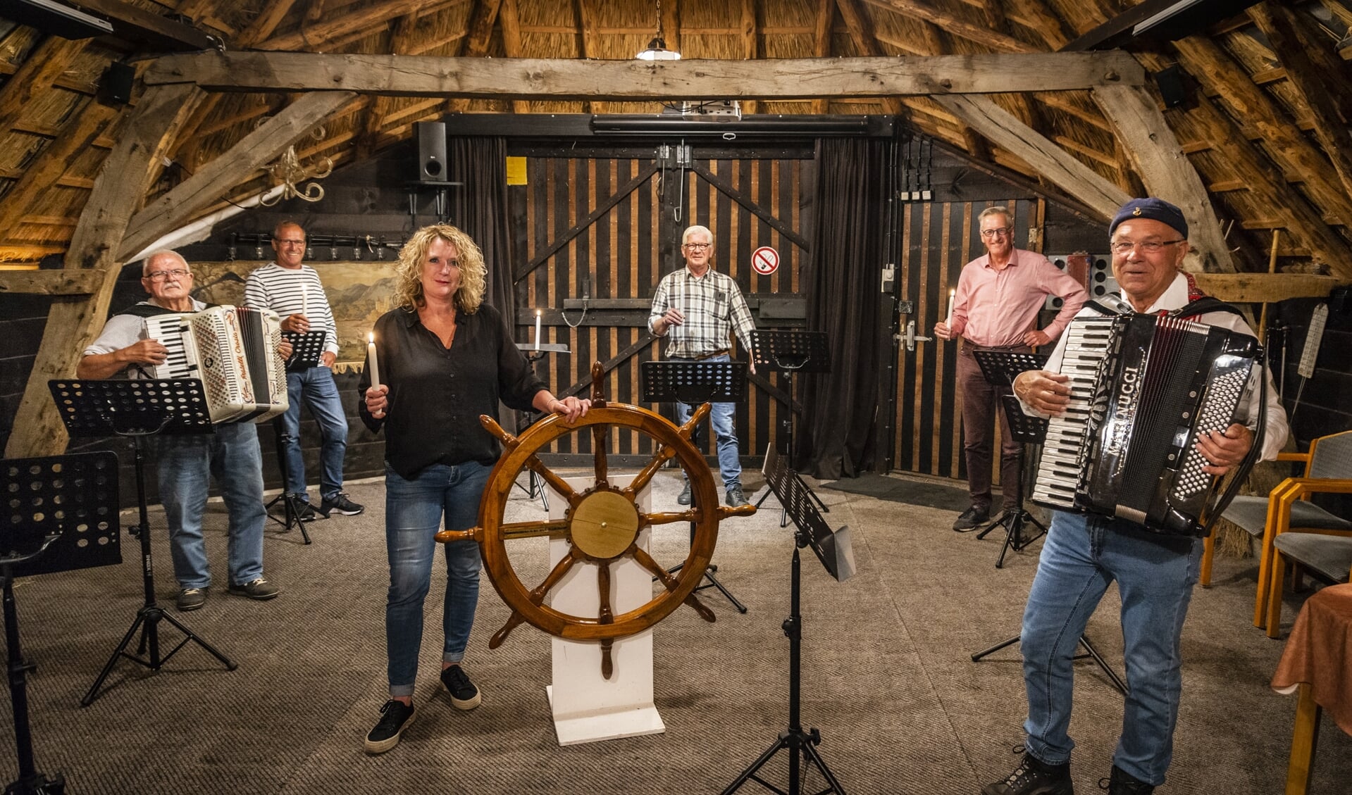 De harde kern van Shantykoor Stroe Ahoy met dirigent Anneke Boersma achter het stuurwiel. ,,De witte kaars is voor de coronaslachtoffers, onze steun aan de zorg en de hoop dat we weer snel mogen beginnen.''