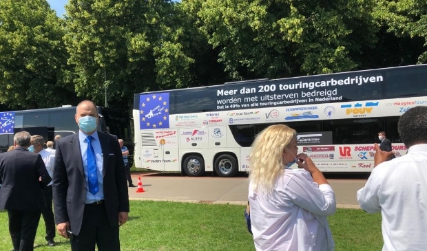 Simon van Kooten van Van Kooten Reizen voor de dubbeldekker met logo's van alle deelnemende touringcarbedrijven.