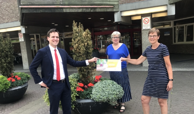 Carla van Houte en Maggy Wijffels overhandigen het eerste lot aan Wethouder Marijn van Ballegooijen.