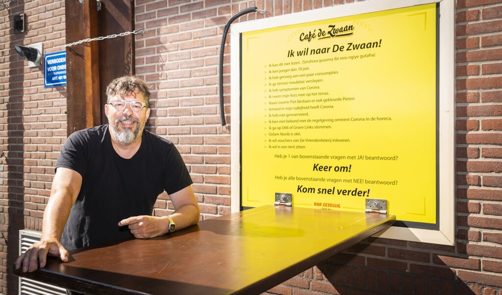 Thomas Bouw op het terras van zijn Cafe De Zwaan, voor de poster met 'huisregels''. 