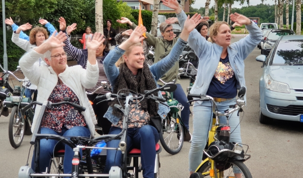 Juf Gerda Zwanenburg, links op de duofiets, swingt mee met collega's tijdens een optreden.