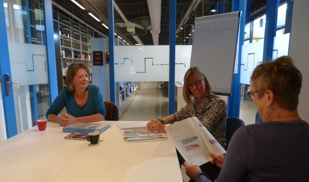 Trees (rechts) krijgt tekst en uitleg van taalmaatje Nathalie Reesink. Annelies Berk (links), coördinator van Taalhuis Ede, kijkt mee.