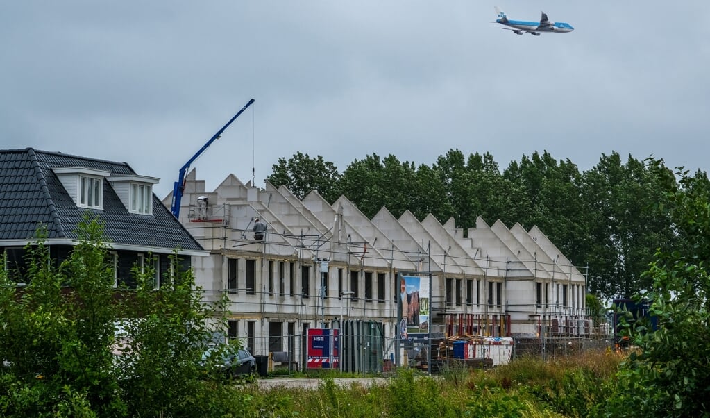 De spagaat van woningbouw en luchtvaart in beeld op het Nassaupark, Terwijl arbeiders bezig zijn, komt er laag een vliegtuig over. 