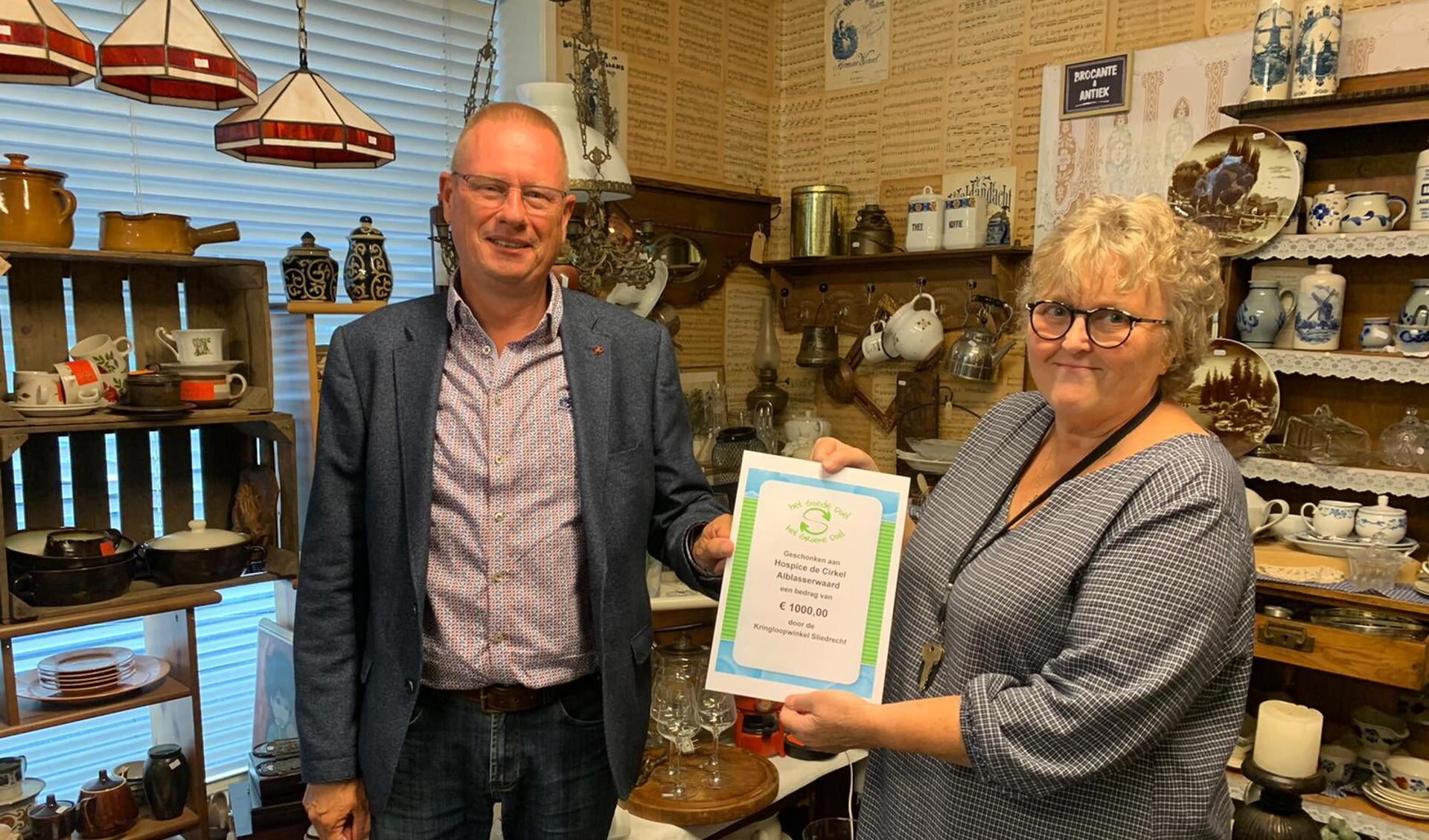Uit handen van Bartha Visser (Kringloopwinkel Sliedrecht) ontvangt Nico van der Veen (Stichting vrienden van hospice De Cirkel) een cheque van 1000 euro.