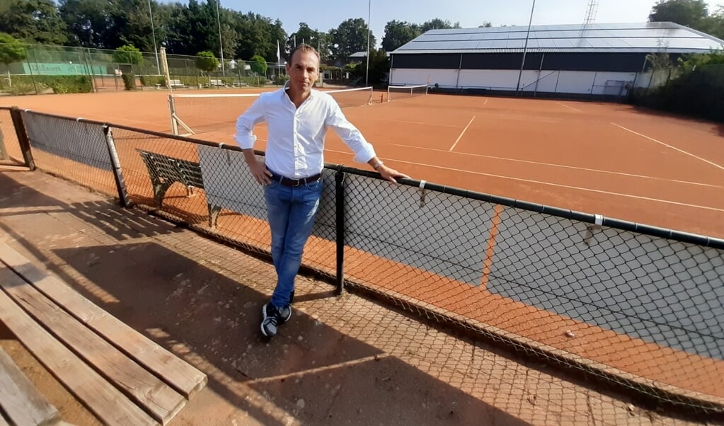Detlef Meijer poseert op het tenniscomplex van LTV Leusden. Achter hem is het dak van de tennishal zichtbaar waarop 300 zonnepanelen werden geplaatst. 