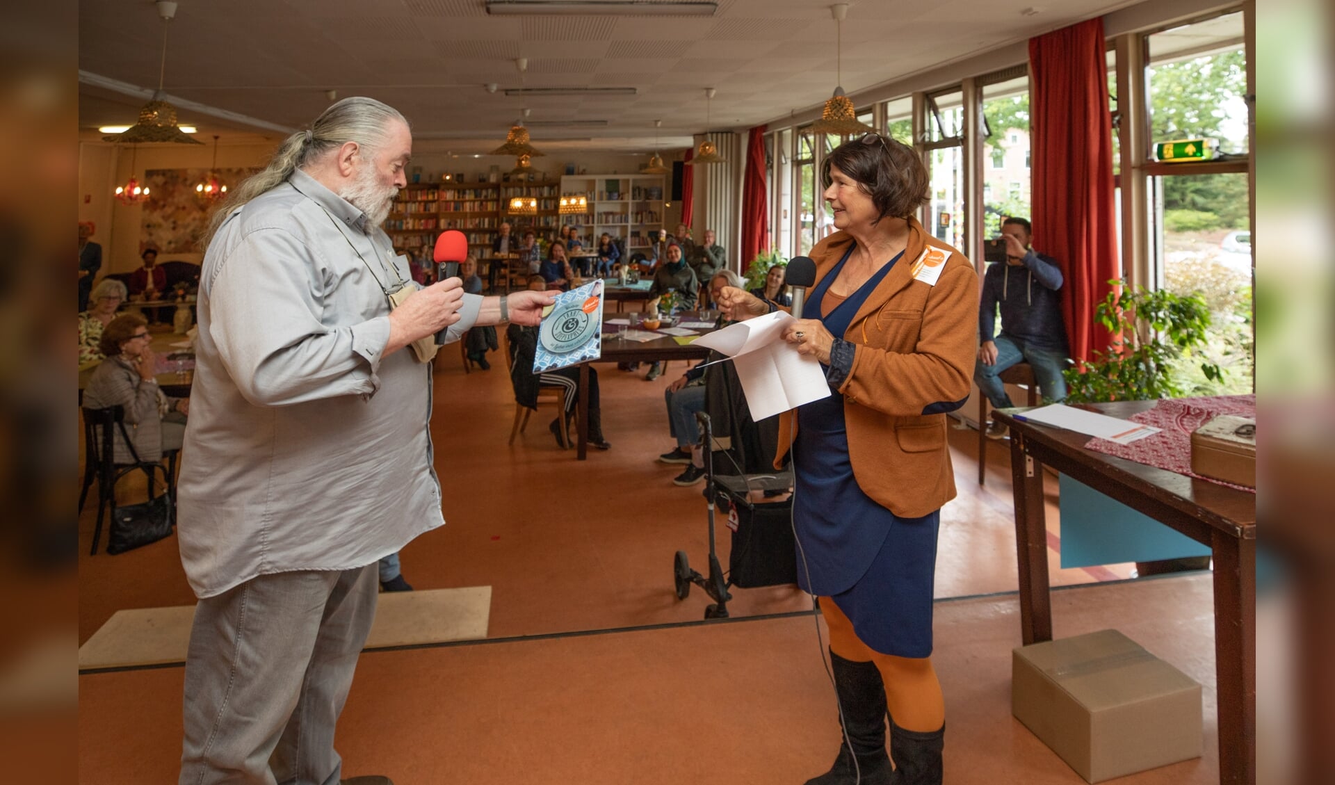 Marjo Stam reikt het eerste Lokaal-O kookboek uit aan Koos Rooyen, gast van het eerste uur van Lokaal-O.  