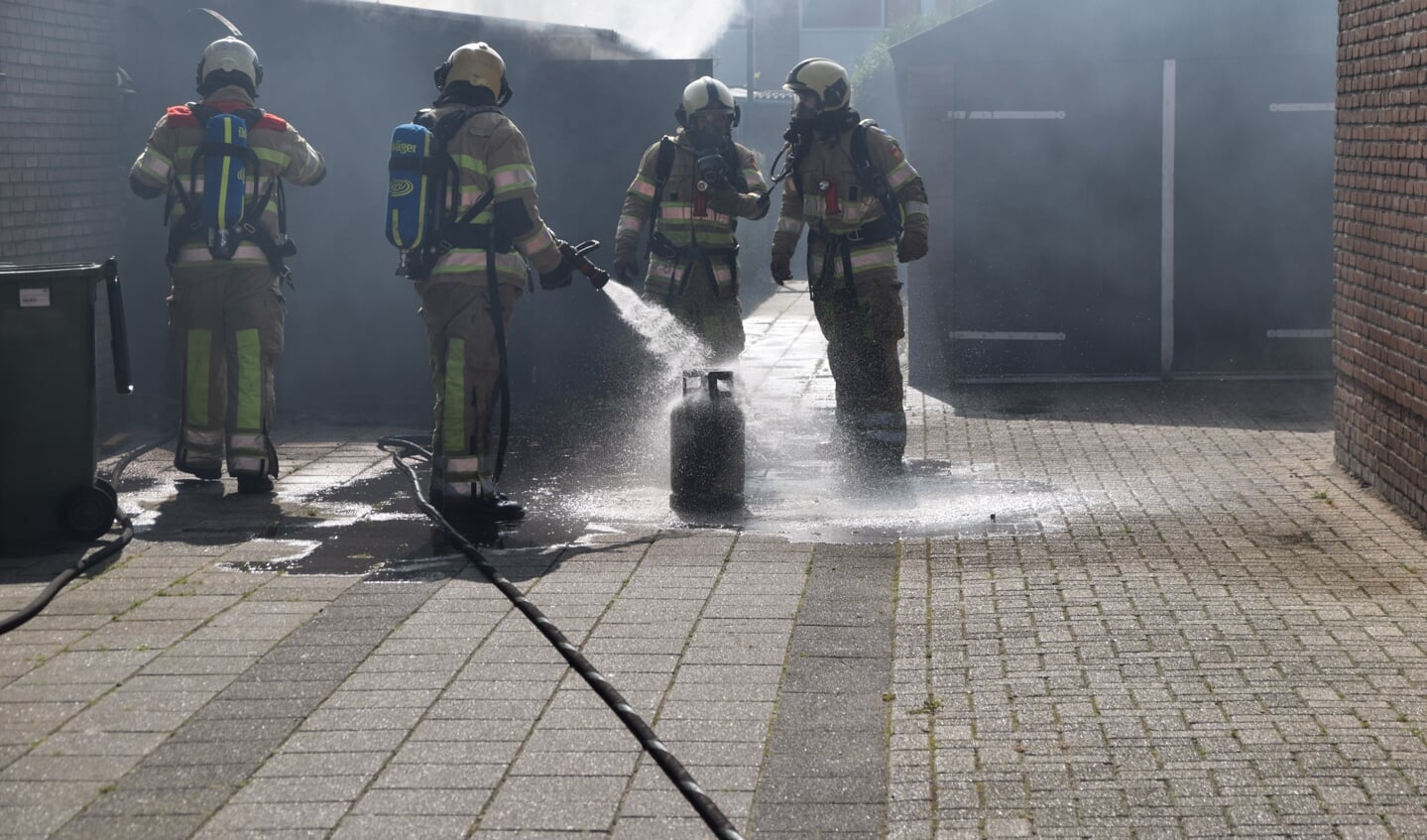 Brandweermannen koelen de gasfles die in de brandende schuur stond.