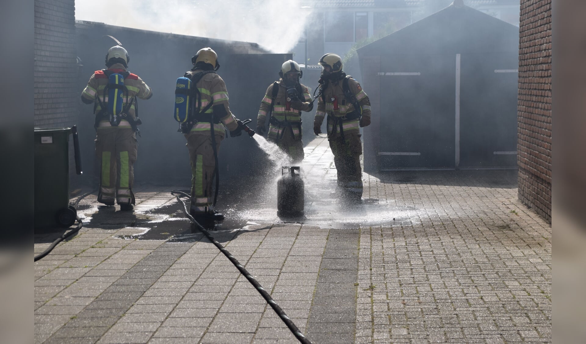 Brandweermannen koelen de gasfles die in de brandende schuur stond.