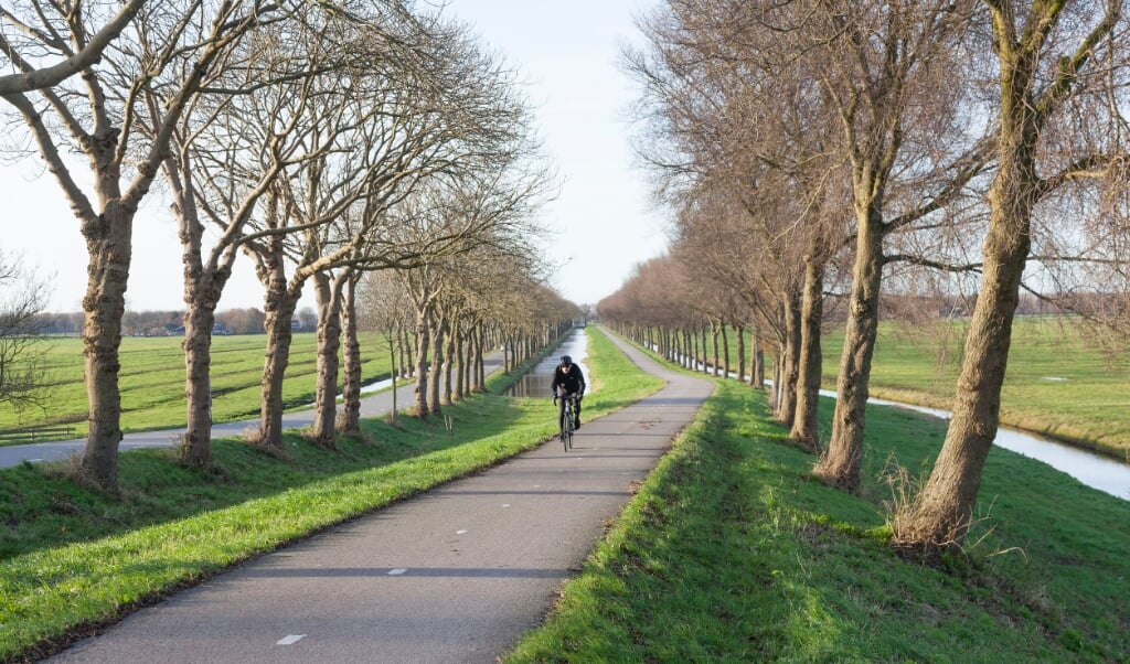 Fietser klimt dijk van de polder Purmer ten noorden van Amsterdam in Nederland op fietspad.