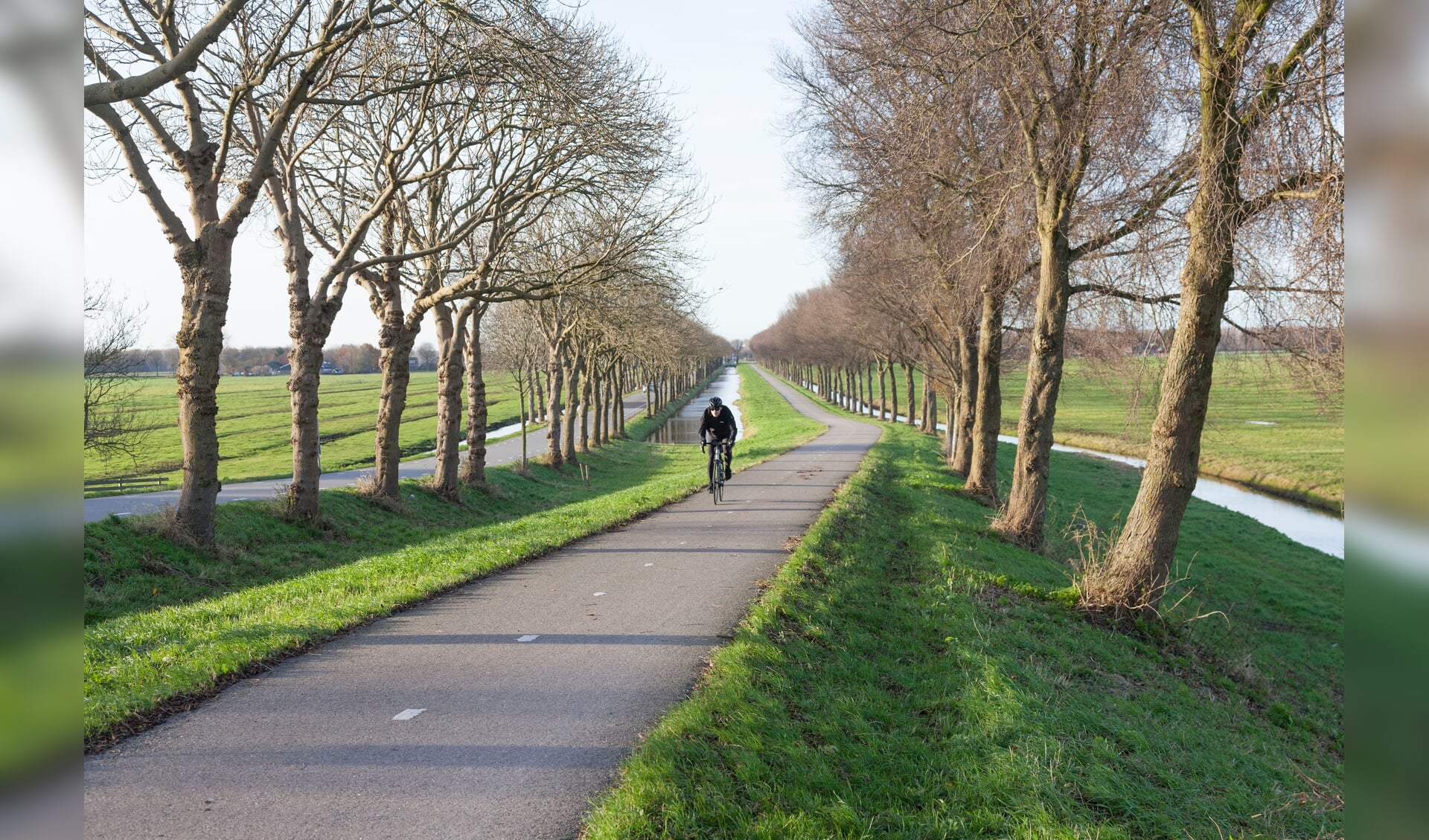 Fietser klimt dijk van de polder Purmer ten noorden van Amsterdam in Nederland op fietspad.
