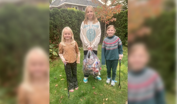 Sammie en Guusje staan met de plastic-raper in hun hand, Kiki houdt de tas met afval vast.