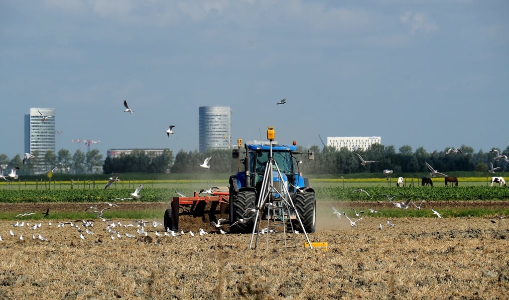 Een mooi beeld van de ontwikkeling in Haarlemmermeer. Een boer werkt met een tractor terwijl verderop Hoofddorp oprukt.  
