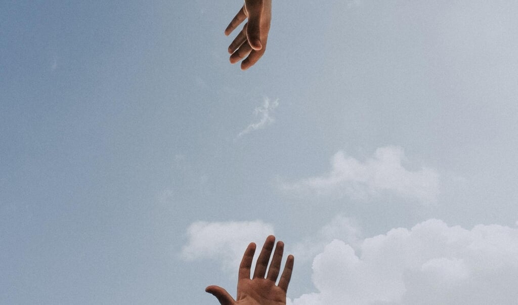 Twee handen reiken naar elkaar in de lucht.