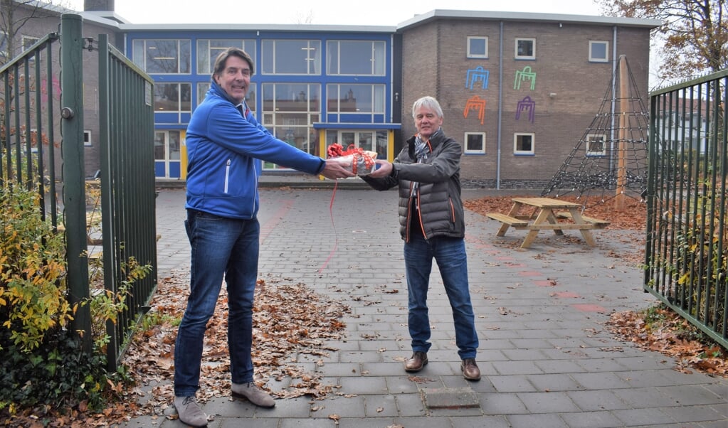 Hugo Prakke (l) overhandigt het presentje aan directeur Jan Visscher op het schoolplein van Guido de Brès.