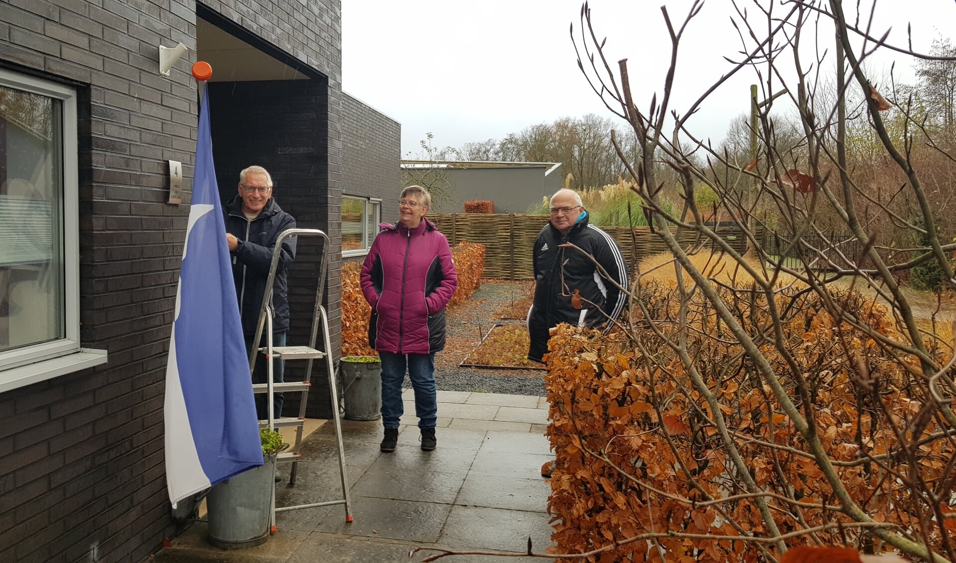 Marianne Krens en Cees Vonk kijken toe als Jaap van Donselaar het symbool van Burgerinitiatief, de vlag Scherpenzeel Zelfstandig, van zijn gevel haalt. 
