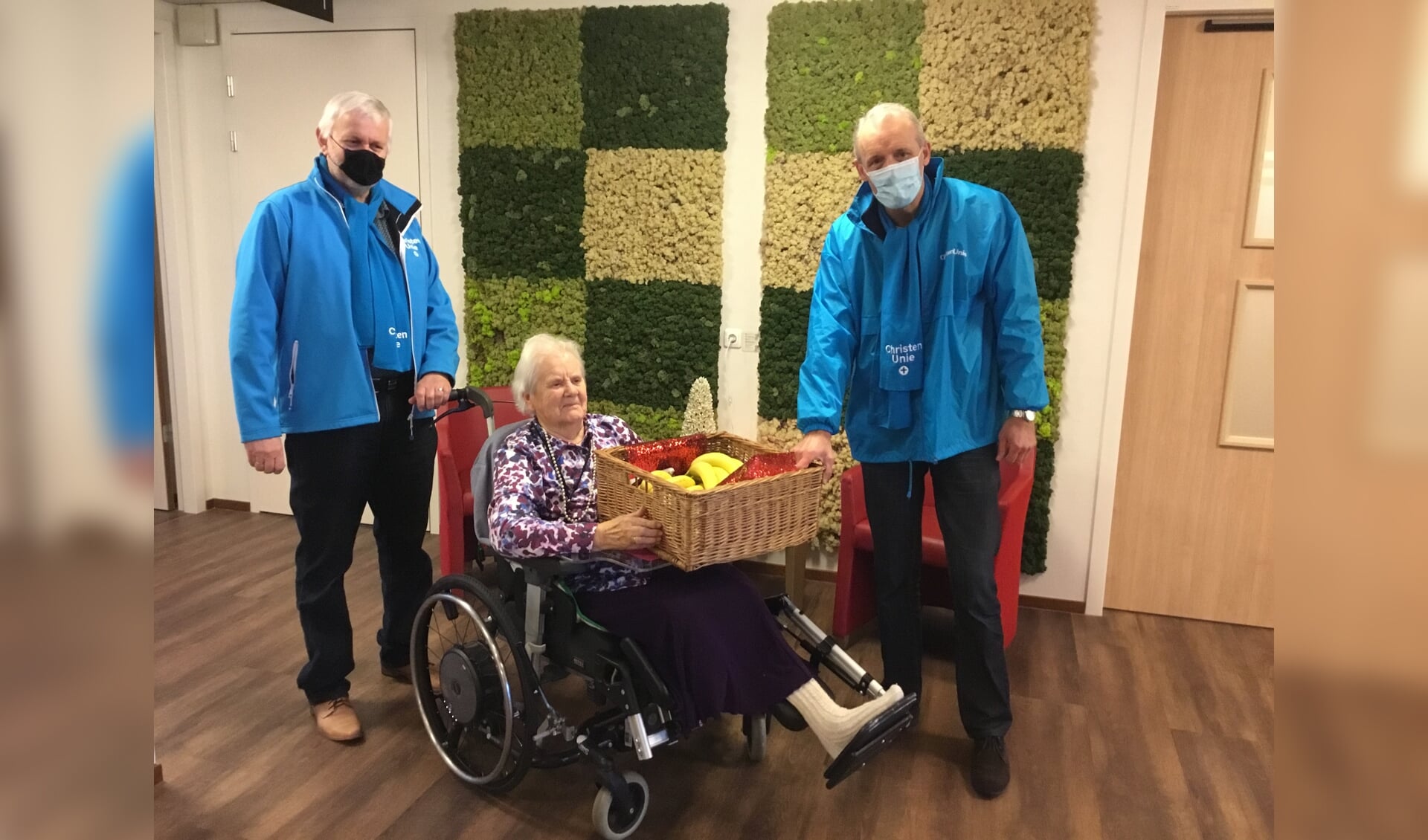 ChristenUnie raadsleden Wim IJzerman en Willem Pors overhandigen een grote mand met fruit aan bewoner van de Tiendwaert mw.van Houwelingen.e 