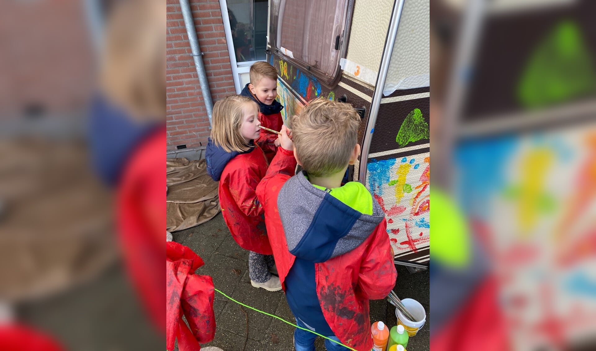 Drie leerlingen van groep 1/2 verven netjes en geconcentreerd de caravan waar Sinterklaas vakantie in mag vieren