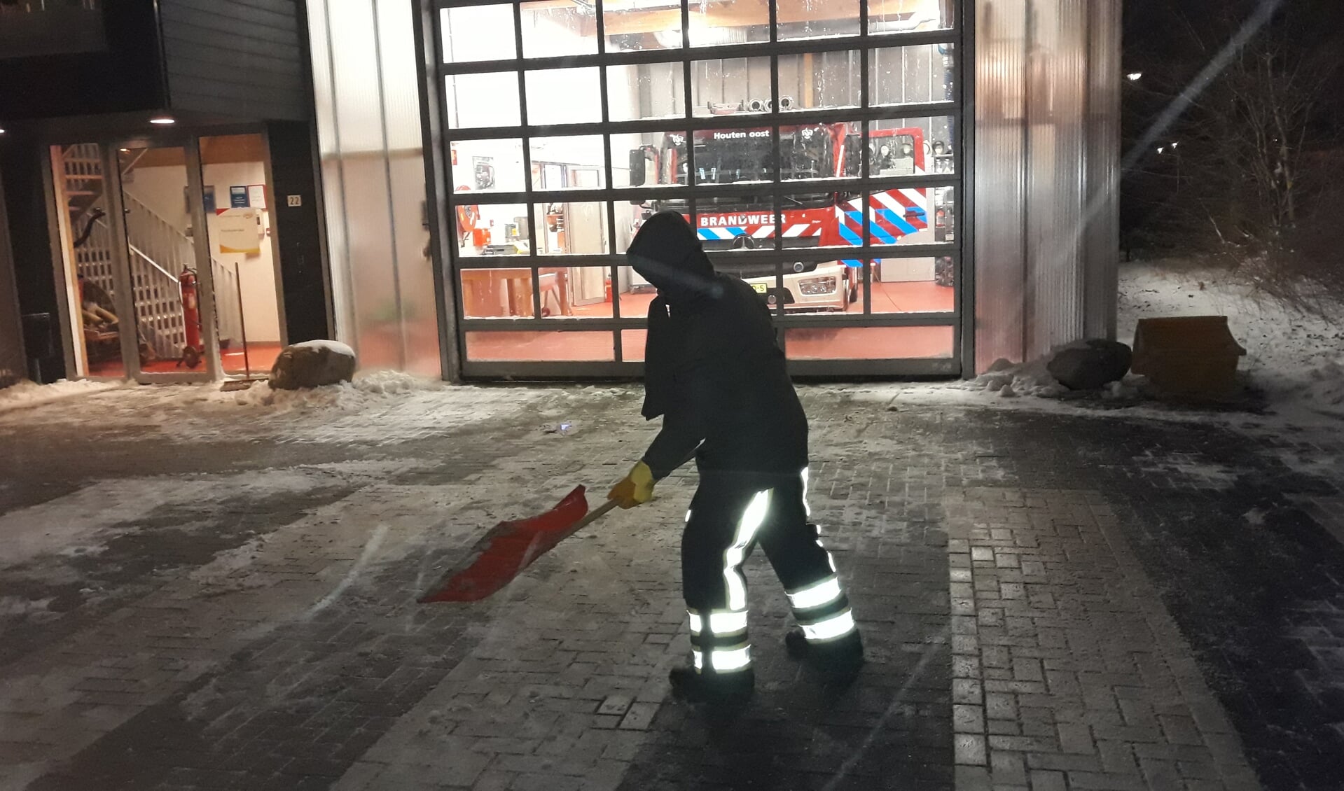 Vrijwilliger strooit zout voor de brandweerpost Oost na sneeuw te hebben weggeschoven.