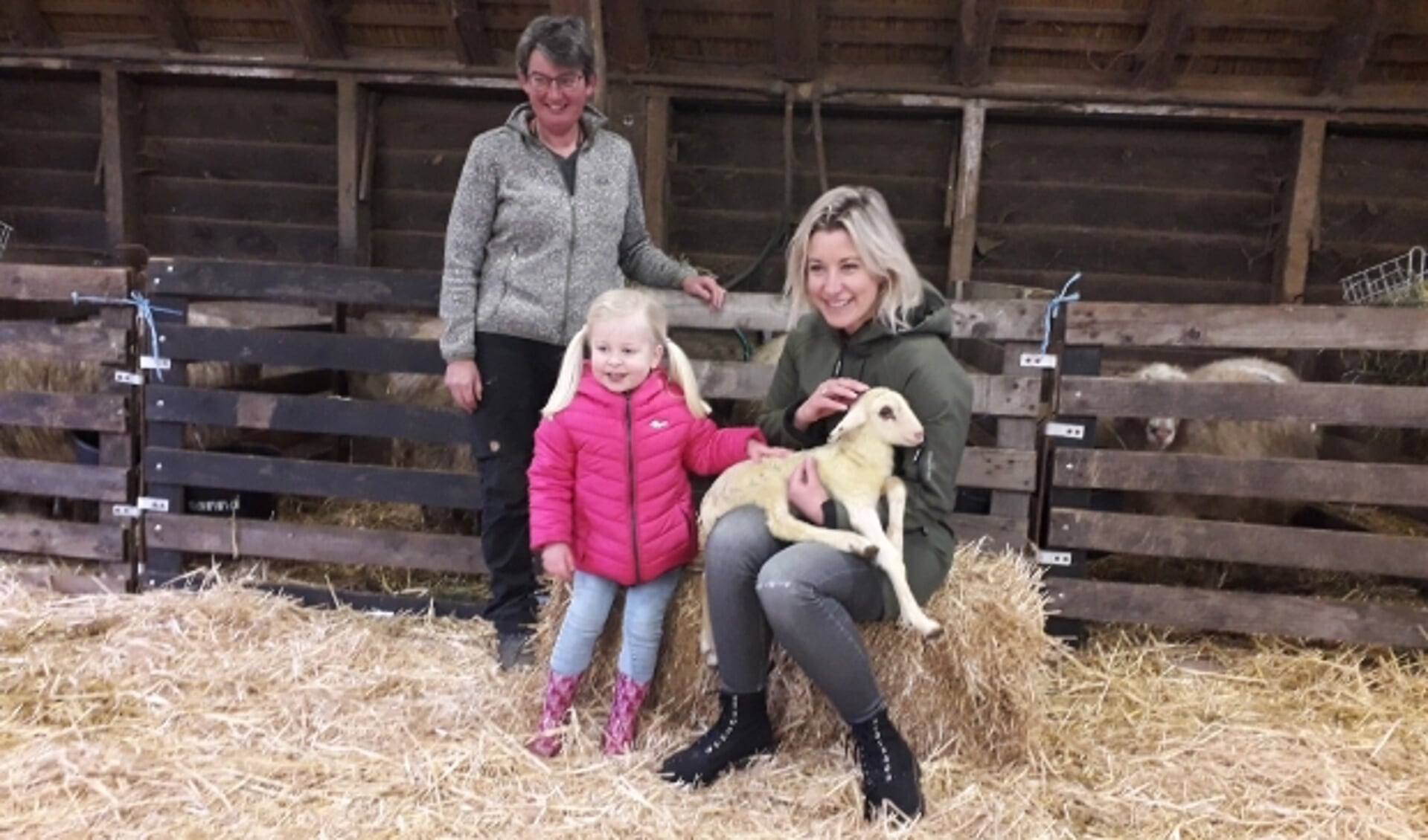 Carrie ten Napel met haar dochtertje met het eerste lammetje Max. Herder Marion Derks kijkt toe.