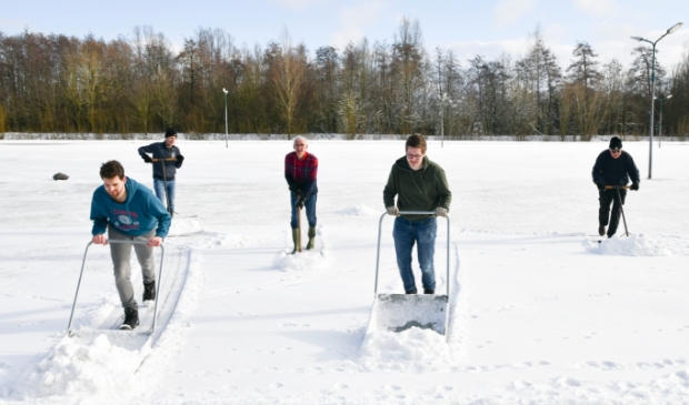 <p>Met man en macht wordt de ijsbaan sneeuwvrij gemaakt, zodat het ijs sneller kan aangroeien.</p>