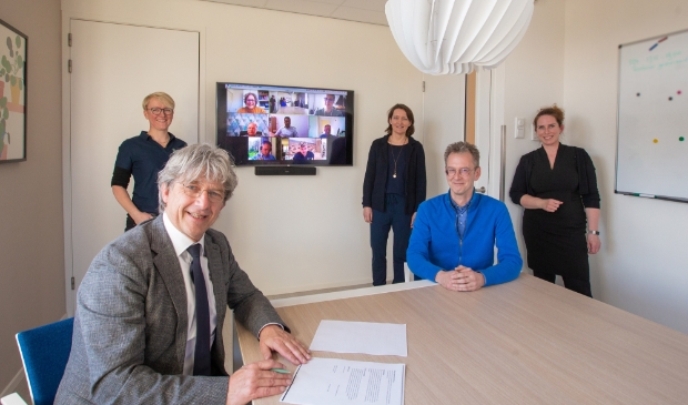 Wethouder Bert Koops en voorzitter van de huisartsengroep Dider Vermaas ondertekenen de intentieverklaring. Achteraan van links naar rechts huisartsen Ineke Weenink, Anouk Bettman en Marieke de Vries en de online aanwezige huisartsen.