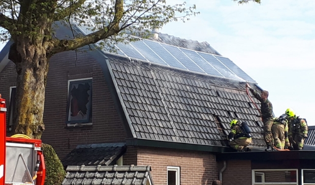 <p>Terwijl net gearriveerde brandweerlieden dakpannen verwijderen, houdt een militair met een tuinslang het dak nat.</p>