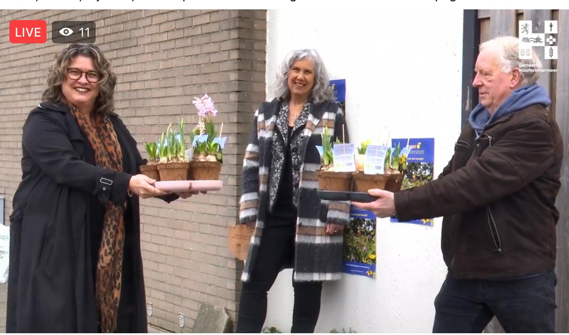 Bewoner van in Overbos Jan Havenaar krijgt van wethouder Steffens enkele plantjes voor zijn geveltuin. NMCX-directeur Arjanne Lagendijk kijkt toe.  