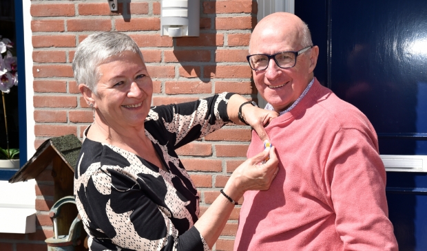 <p>Echtgenote Ria speldt de versierselen op bij Jaap van den Broek, zojuist benoemd tot Lid in de Orde van Oranje Nassau.</p>