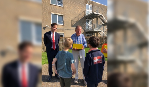 2 leerlingen van de Roelof Venemaschool overhandigen samen met Wethouder Van Ballegooijen een pakketje aan een 88-jarige bewoner van Nieuw Vredenhoven