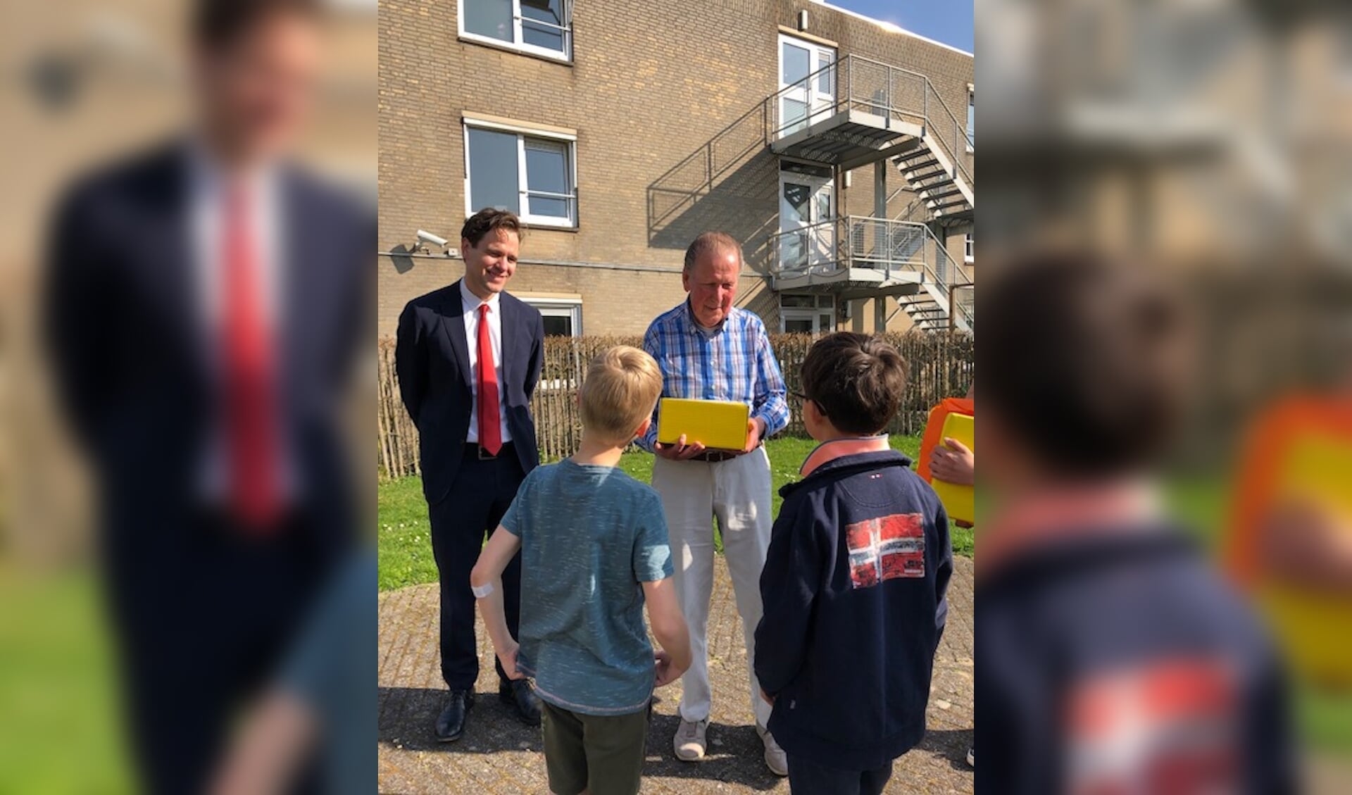 2 leerlingen van de Roelof Venemaschool overhandigen samen met Wethouder Van Ballegooijen een pakketje aan een 88-jarige bewoner van Nieuw Vredenhoven