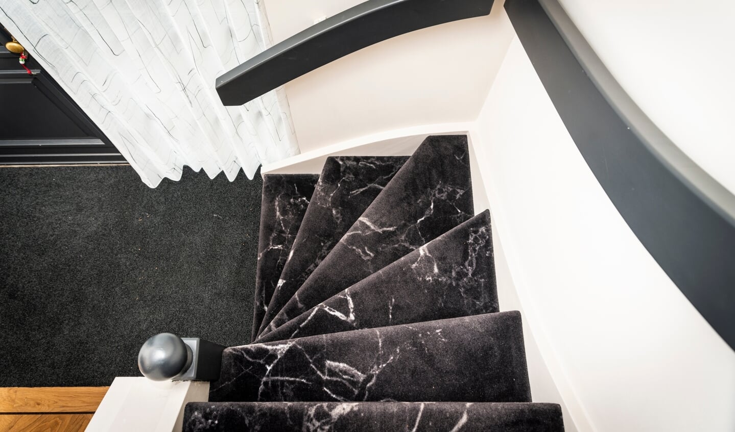 De trap is bedekt met zwart tapijt, voorzien van een marmerachtige print.