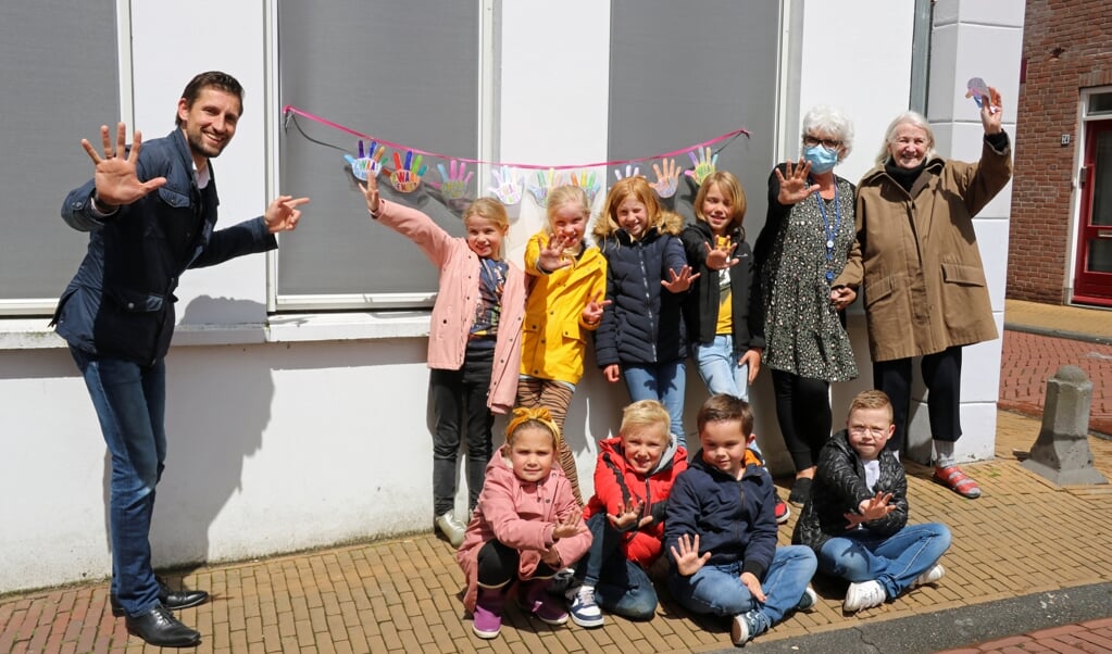 Wethouder Kraaijeveld (links) samen met kinderen van de Jenaplanschool, initiatiefneemster van de zwaaistickers Tineke Advokaat (met mondkapje) en een van de bewoners van verpleeghuis Molenhoek (geheel rechts)