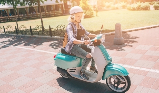 Young cheerful girl driving scooter in in city. Portrait of a young and stylish woman with a moped.