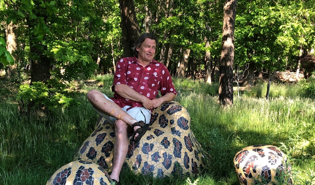 Kunstenaar Erik Wuthrich zittend op een kunstwerk in zijn bossige tuin.