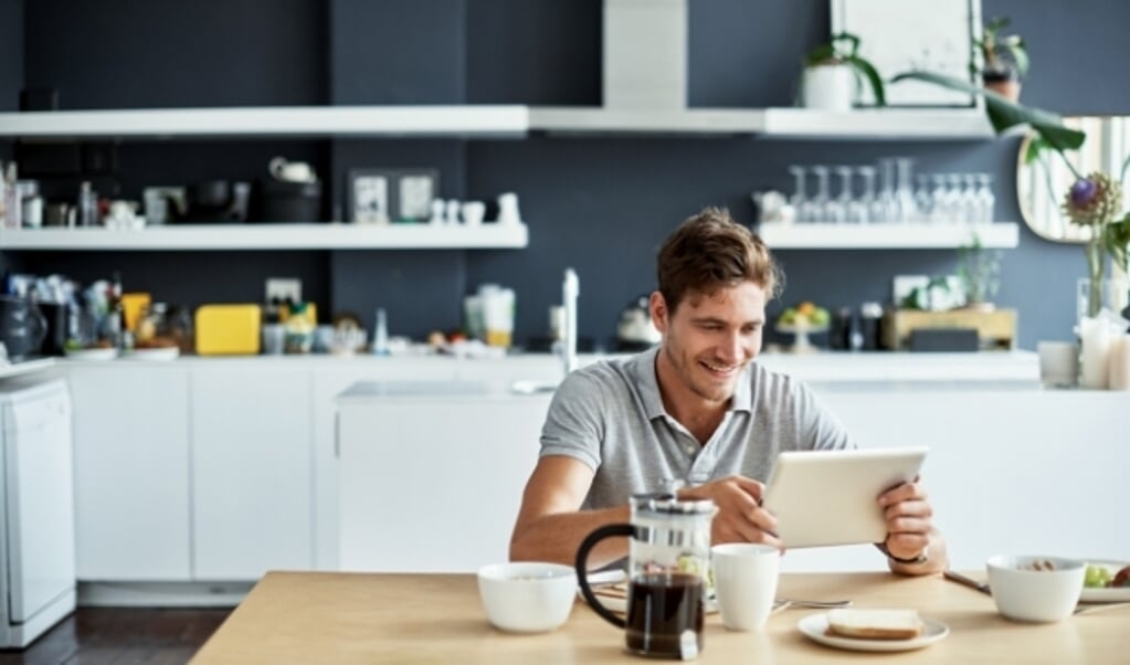 Shot of a happy young man using his tablet while enjoying breakfast at home