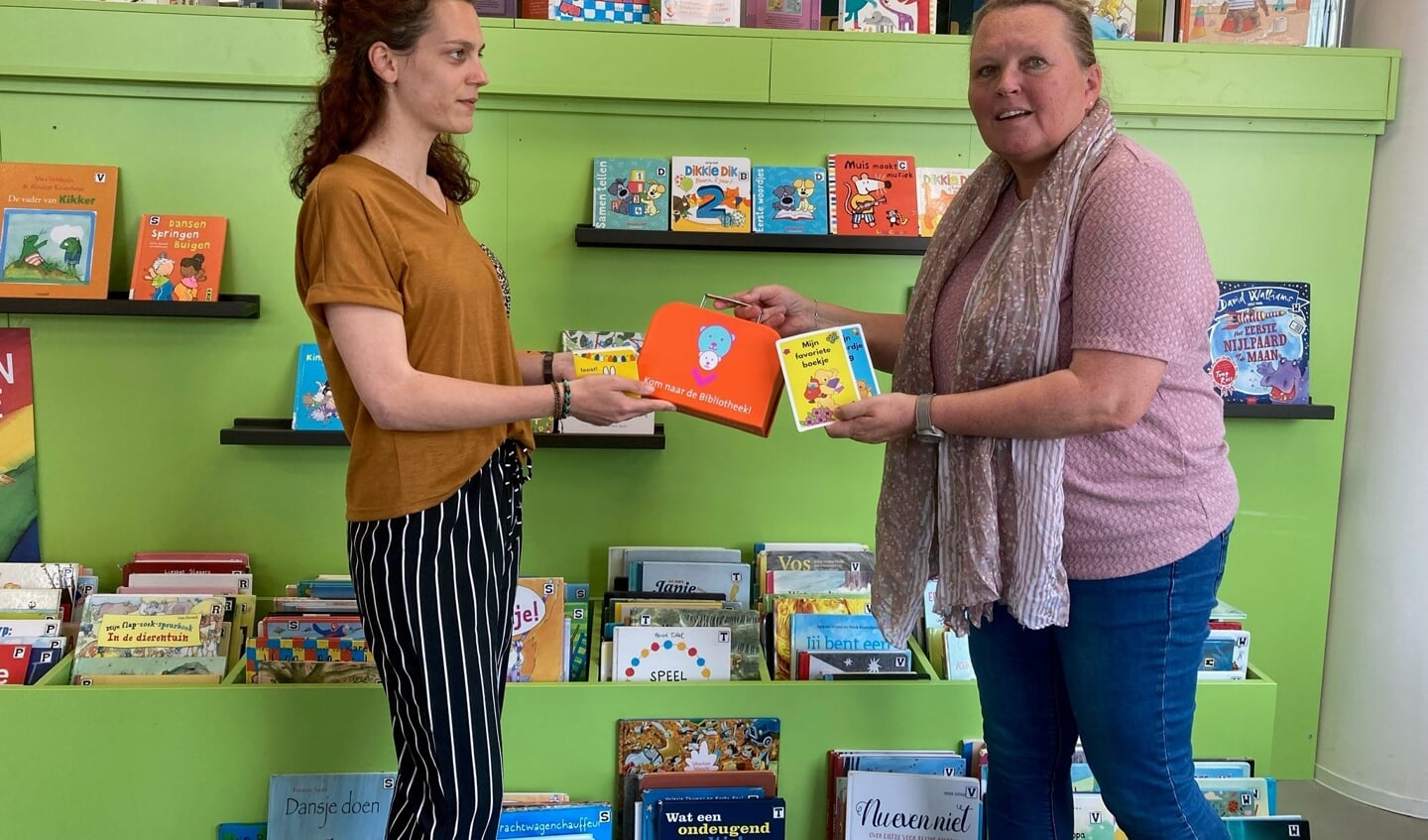 Liesbeth Versteeg van de Bibliotheek Z-O-U-T reikt een BoekStartkoffertje uit en laat de baby- en dreumesboekjes zien in de jeugdhoek van de Bibliotheek.