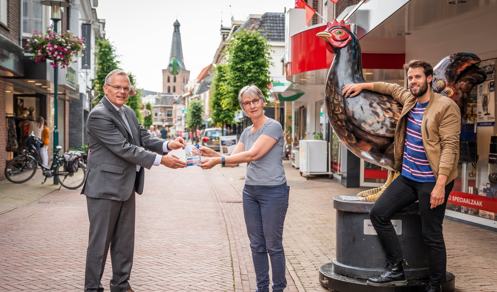 Burgemeester Jan Luteijn (links) krijgt het eerste exemplaar van 'Dit is Barneveld' overhandigd door centrummanager Simone Giele. Rechts op de foto Sander van den Brink.