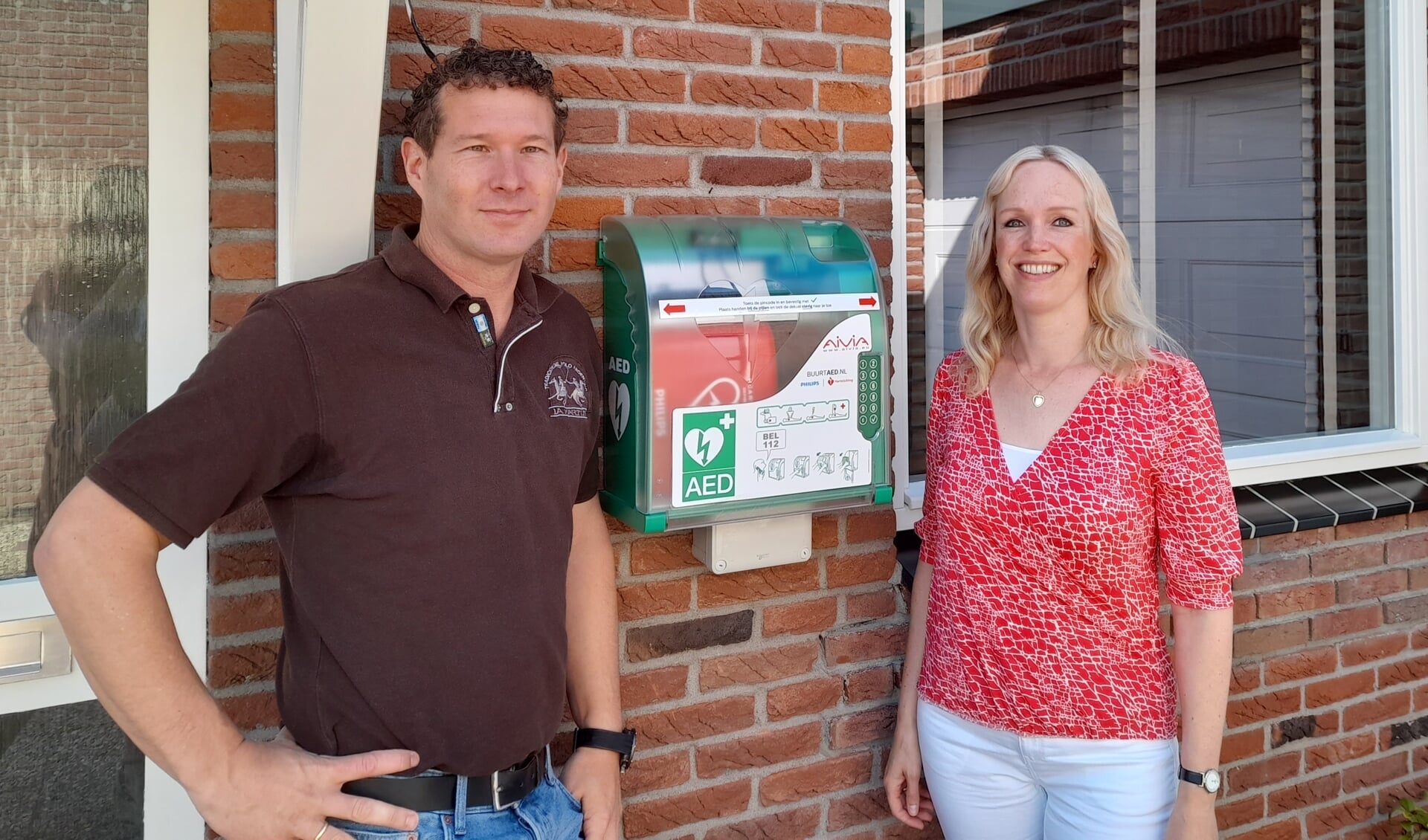 Björn en Aline Schuckmann voor hun woning met aan de gevel een AED. 