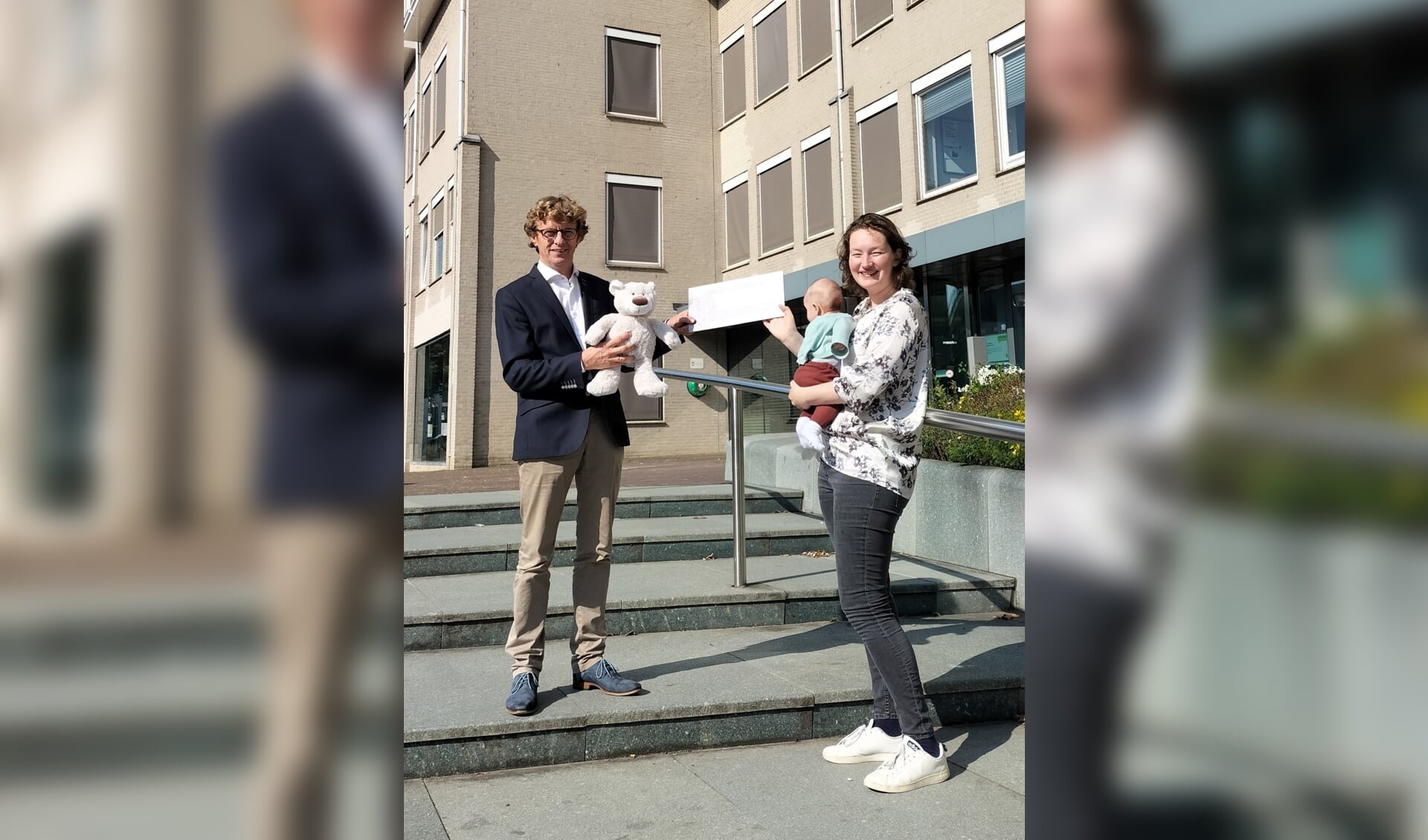 Jorine Rabius ontvangt uit handen van wethouder Jan Overweg een tegoedbon voor de cursus OudersInc. De knuffelbeer is voor baby Bram. 