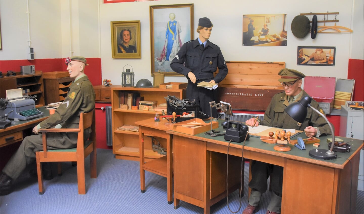 Een werksituatie op een militair bureel met links een kennelijk blije korporaal.