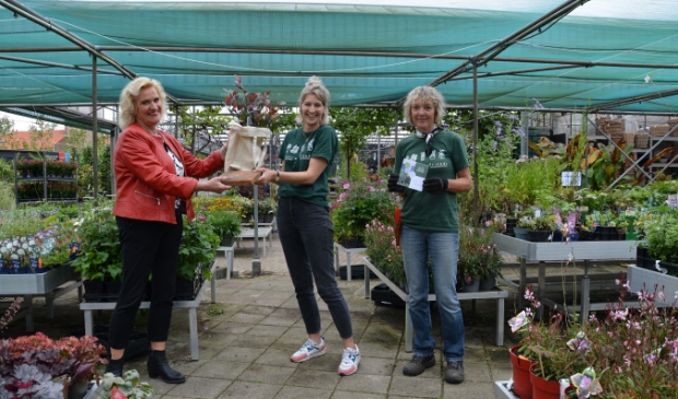 <p>Wethouder Wil Kosterman met tegel, Corienne Merkens van Merkens Tuincentrum met gratis plant in tas en Lianne Peters van Merkens. </p>