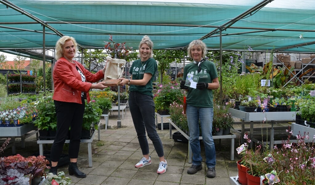 Wethouder Wil Kosterman met tegel, Corienne Merkens van Merkens Tuincentrum met gratis plant in tas en Lianne Peters van Merkens.  