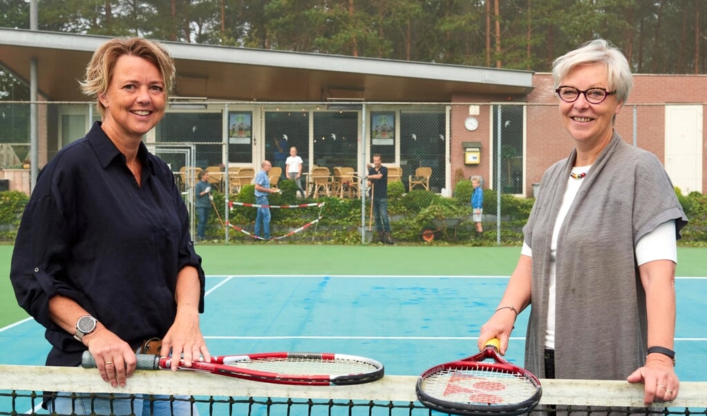 Esther van der Horst (l) en Hennie Brink op de banen van de tennisvereniging Elspeet. In de achtergrond bij de kantine zijn vrijwilligers hard aan het werk met het wekelijkse onderhoud en om alles in orde te maken voor het komende toernooi.