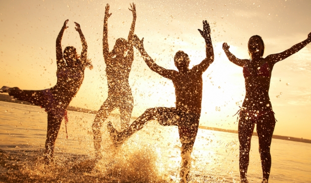 group of happy young people dancing and spraying at the beach on beautiful summer sunset