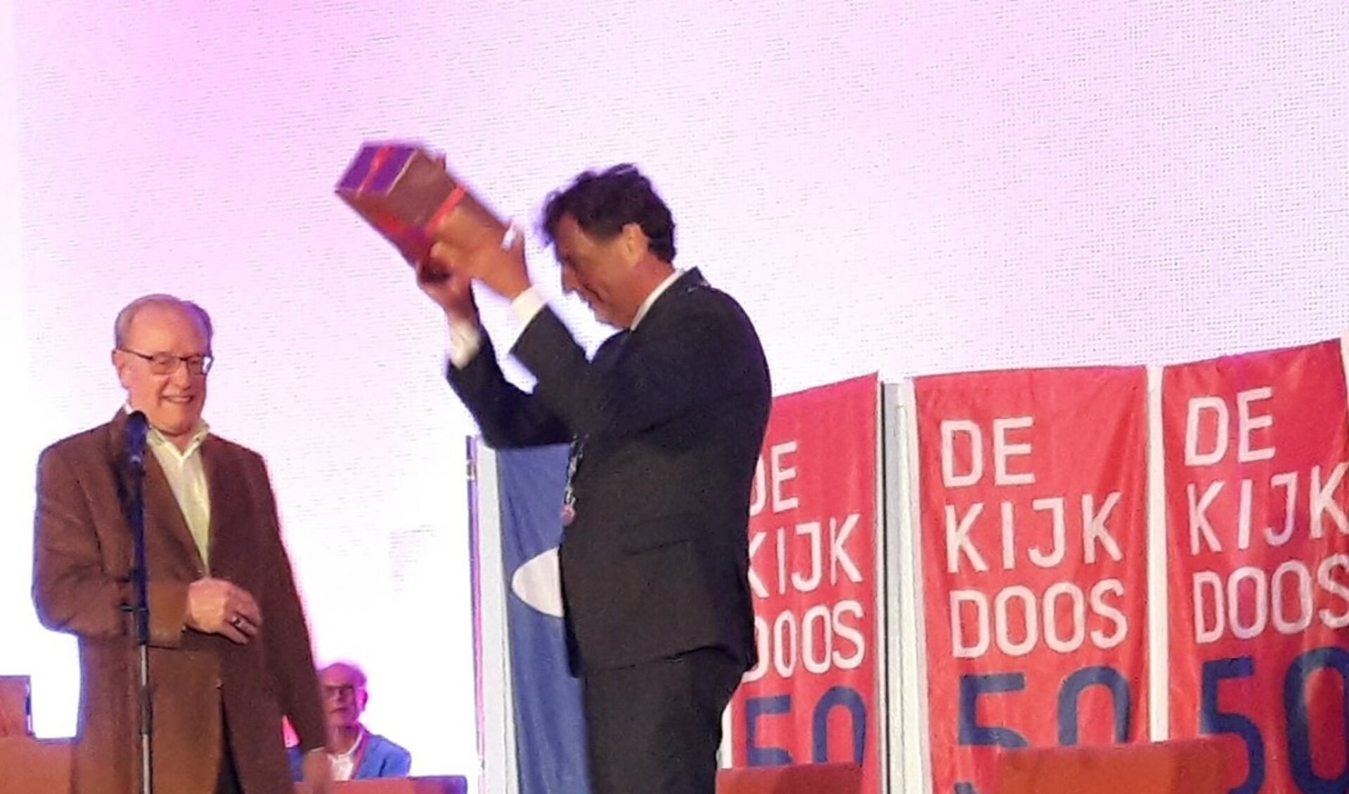 De burgemeester krijgt het Kijkdoos jubileumboek van Jan van den Hazel en houdt het juichend omhoog