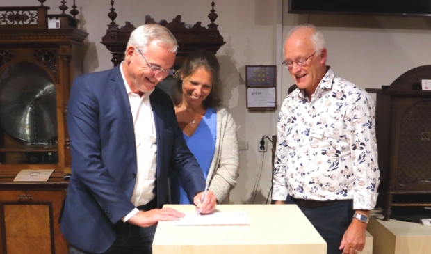 De heer Hulsbergen tekent het schenkingsformulier van de vleugelpianola onder toezined oog van zijn echtgenote en de directeur van Het Kijk en Luistermuseum.
